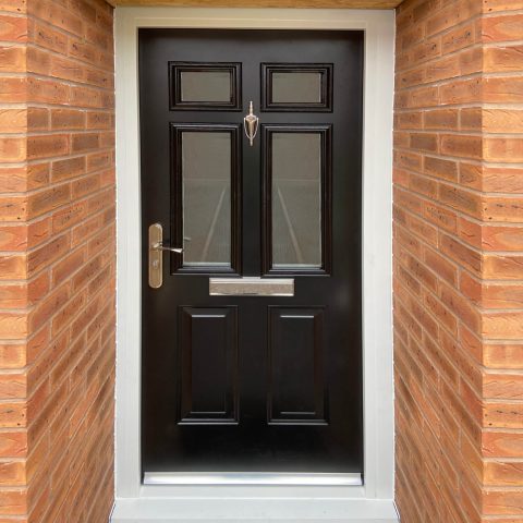 Jet black panelled front door with knocker, letterbox and rain deflector